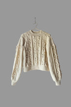 Beige knitted sweater on a wooden ladder against a white wall