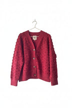 Red textured cardigan hanging on a wooden ladder against a white wall.