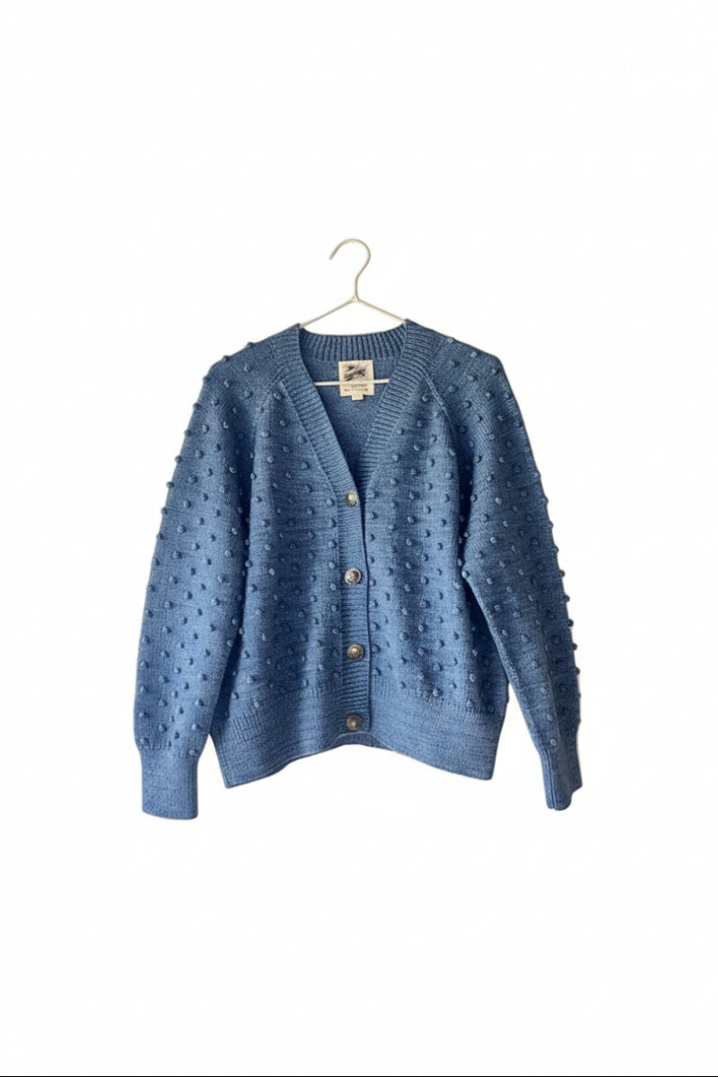 Blue knitted cardigan hanging on a wooden ladder against a white wall.